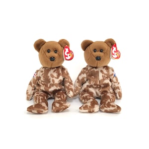 Puede incluir: Dos osos de peluche Beanie Baby de color marrón camuflaje con etiquetas Ty rojas y blancas. Los osos llevan tela con estampado de camuflaje.