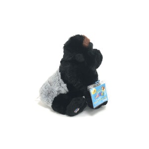 May include: A plush gorilla toy with black fur, gray accents, and a brown face. The toy has a tag attached. The gorilla is sitting down and facing to the right.