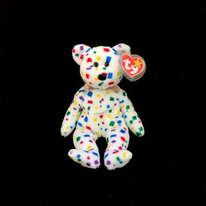 May include: White beanie baby bear with a colourful confetti pattern. The bear has a red Ty heart tag with a white star.