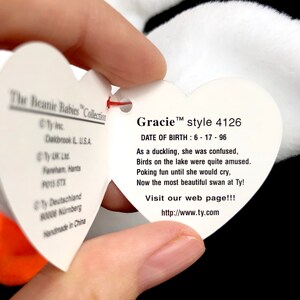 Op de afbeelding: Een wit hartvormig label van The Beanie Babies Collection, met de naam "Gracie" en stijlnummer 4126. Het label bevat een gedicht en een websiteadres. Het label wordt door een persoon vastgehouden.