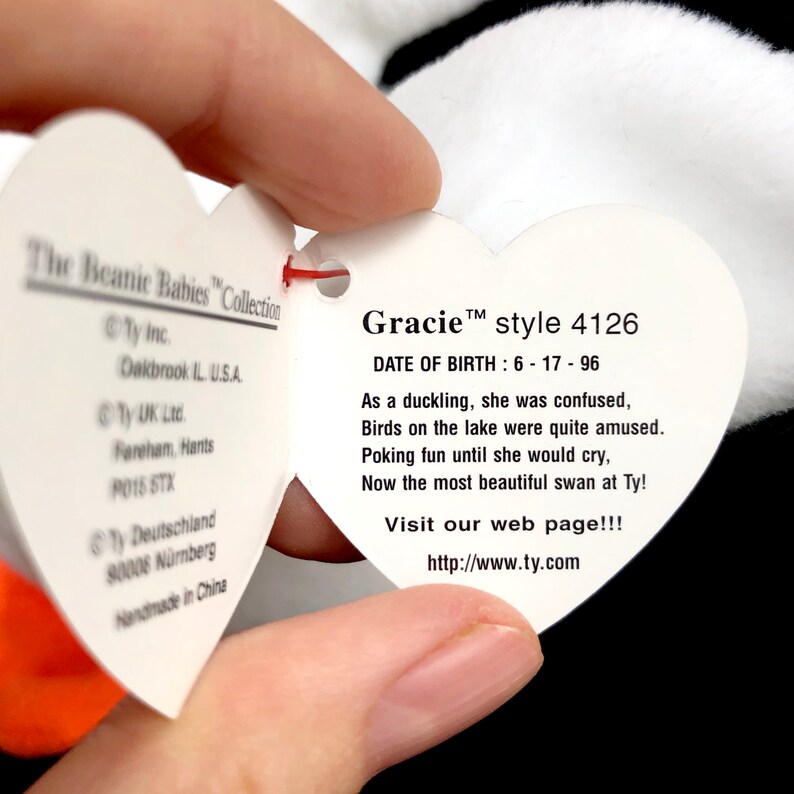 Op de afbeelding: Een wit hartvormig label van The Beanie Babies Collection, met de naam "Gracie" en stijlnummer 4126. Het label bevat een gedicht en een websiteadres. Het label wordt door een persoon vastgehouden.