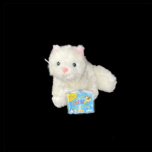May include: White plush cat Webkinz toy with pink ears and blue eyes. The toy is sitting on a white surface and has a Webkinz tag attached to it. The tag is blue and white and has the Webkinz logo on it. The tag also says "Discover a virtual world" and "Ganz".