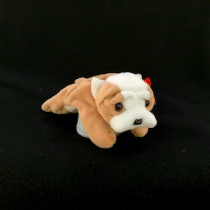May include: A brown and white plush bulldog with a red tag. The bulldog is lying on its side with its head resting on its paws.