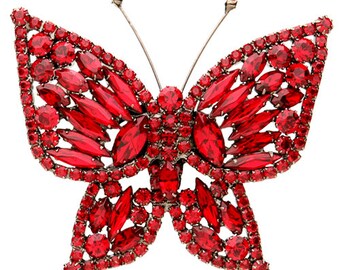 Puede incluir: Broche de mariposa roja, incrustado con numerosas piedras preciosas rojas. El broche presenta un diseño detallado con un marco de metal plateado y delicadas antenas. Las piedras preciosas son de varias formas y tamaños, creando un efecto brillante.