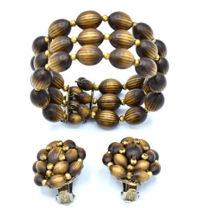 May include: A vintage jewelry set featuring a multi-strand bracelet and matching clip-on earrings. The bracelet and earrings are made of dark brown, oval-shaped beads with gold-colored accents. The beads have a striped pattern.