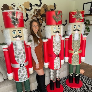 May include: Three large, decorative nutcrackers. Each nutcracker has a red coat, a white beard, and a black mustache. The legs are green and plaid. The nutcrackers stand on red circular bases and have red hats decorated with greenery.