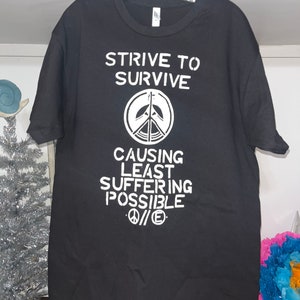 May include: Black t-shirt with white text that reads "Strive to Survive Causing Least Suffering Possible" with a peace sign symbol.