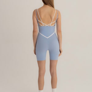 Puede incluir: Un conjunto deportivo de una pieza azul claro con tirantes blancos y un diseño en forma de V en la parte delantera. El conjunto está hecho de un material elástico y cómodo, perfecto para yoga, pilates u otros entrenamientos.