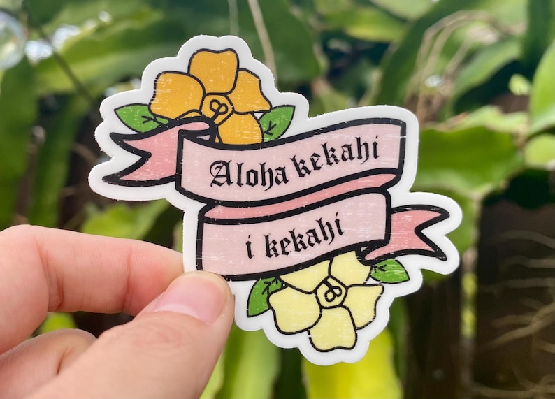 May include: A pink and white sticker with yellow flowers and the text "Aloha kekahī i kekahī".