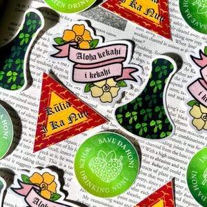 May include: A collection of colorful stickers with Hawaiian and tropical themes. The stickers feature phrases like "Aloha kekahi i kekahi", "Kūlia i ka Nuʻu", and "Save Da Honī When Drinking Noni".