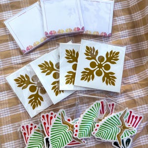 May include: A set of stickers featuring a gold floral design and a green and red geometric design. The stickers are packaged in clear plastic bags.