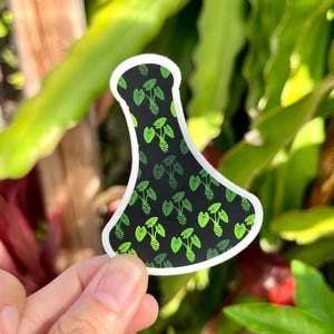 May include: A black and green vinyl sticker of a bottle with a leafy pattern. The sticker is shaped like a bottle and has a white outline.