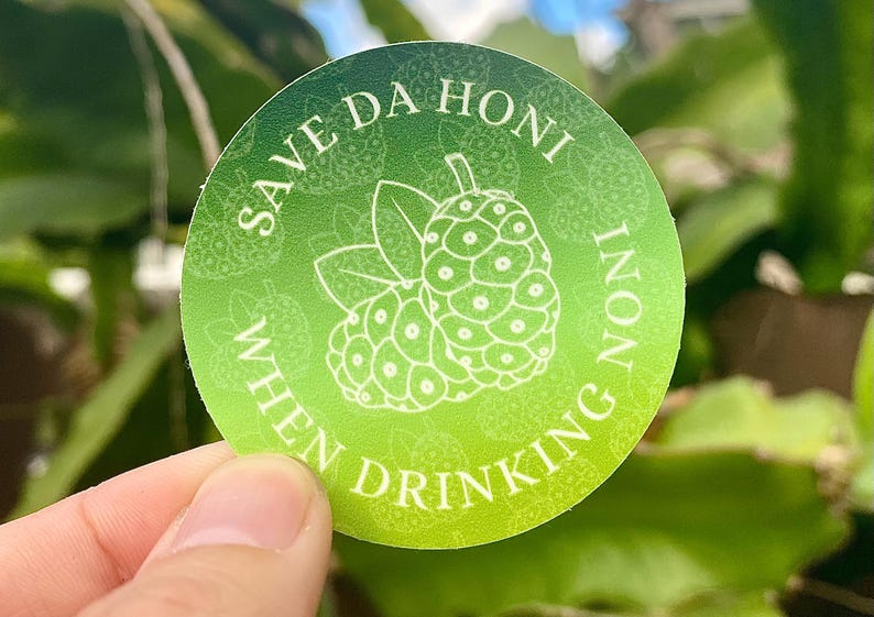 May include: A green and white round sticker with the text "Save Da Honi When Drinking Noni" and a white illustration of a noni fruit.