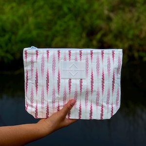 May include: White zippered pouch with a pink and white floral pattern. The pouch has a white label with the text "STAMPED DESIGNS" on it.