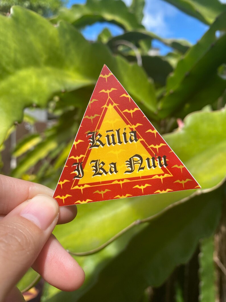 May include: A red triangular sticker with a yellow center and a pattern of red bats. The sticker says "Kuli'a I Ka Nu'u" in black lettering.