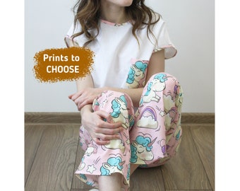 May include: A white short-sleeved t-shirt with a pink unicorn print pocket and pink pyjama pants with a unicorn print. The text "Prints to CHOOSE" is in a brown box.