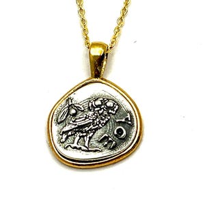 May include: A gold chain necklace with a silver pendant featuring a detailed image of an owl. The pendant is shaped like a coin with a raised edge and the words 'ATHENA' inscribed around the owl