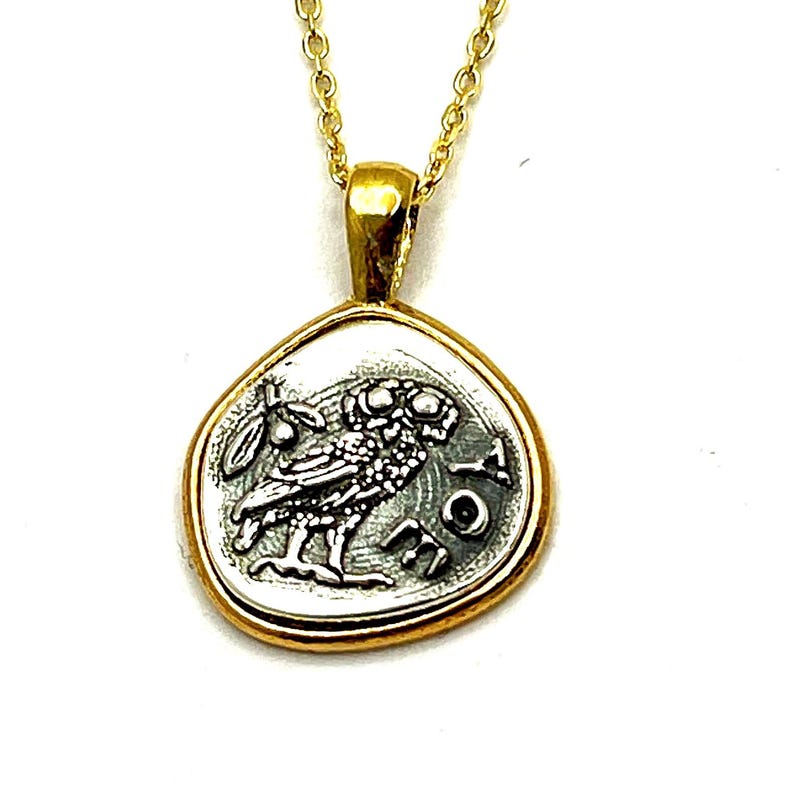 May include: A gold chain necklace with a silver pendant featuring a detailed image of an owl. The pendant is shaped like a coin with a raised edge and the words 'ATHENA' inscribed around the owl