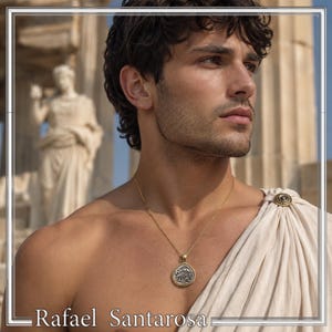 May include: A gold-toned chain necklace featuring a circular pendant with a silver-colored embossed owl design. The necklace is worn with a draped off-white fabric garment secured at the shoulder by a circular gold-toned decorative brooch.
