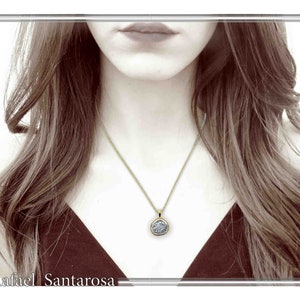 May include: A gold chain necklace featuring a circular pendant with a textured, silver-toned center. The pendant has a smooth gold-colored border and hangs from a delicate gold link chain. The text Rafael Santarosa is visible at the bottom.