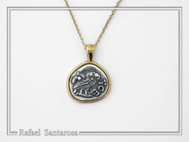May include: A gold-toned chain necklace featuring a circular pendant with a silver-colored center. The pendant displays an embossed owl figure and the Greek letters AOE. The metal has a textured, aged finish throughout the entire piece.