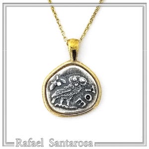 A gold chain necklace with a silver pendant featuring a detailed image of an owl. The pendant is shaped like a coin with a raised edge and the words 'ATHENA' inscribed around the owl.