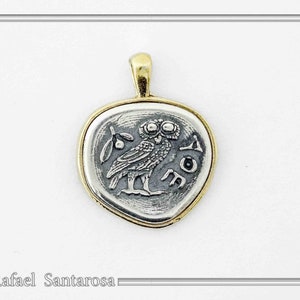May include: A silver-toned pendant with a gold-toned rim featuring an embossed owl design, a small sprig, and the Greek letters AOE. The pendant has a gold-toned bail at the top. The text Rafael Santarosa is visible in the bottom left corner.