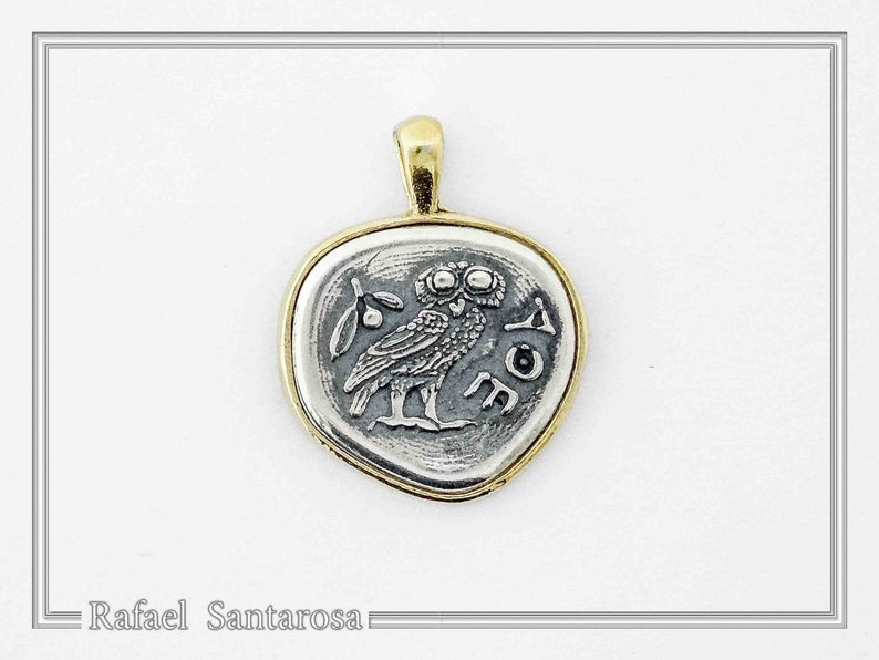 May include: A silver-toned pendant with a gold-toned rim featuring an embossed owl design, a small sprig, and the Greek letters AOE. The pendant has a gold-toned bail at the top. The text Rafael Santarosa is visible in the bottom left corner.