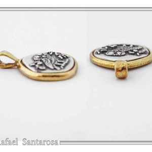 May include: A two-tone pendant featuring a silver-colored oval center with a raised relief design, encased in a smooth gold-colored metal border. The pendant includes a small gold-colored bail at the top for attachment. The text Rafael Santarosa is visible.