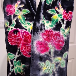 May include: A dark blue velvet scarf with a floral pattern of pink roses and green leaves. The roses are clustered and detailed, set against a white background. The scarf is draped over a mannequin.