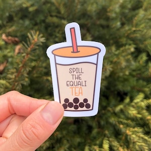Può includere: Un adesivo con una tazza di tè boba a fumetti con la scritta "Spill the Equali Tea". La tazza ha una bevanda marrone chiaro, perle di boba marroni e una cannuccia rossa. La tazza è bordata di bianco e ha un coperchio arancione.