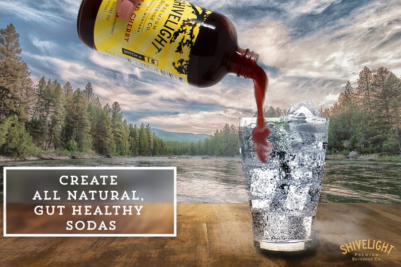 May include: A glass bottle with a yellow label that reads "Hivelight Premium Beverage Co. Wild Cherry" is being poured into a glass with ice. The glass is on a wooden surface with a river and trees in the background. The text "Create All Natural, Gut Healthy Sodas" is on a white rectangle in the foreground.