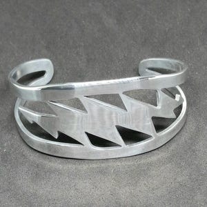 Può includere: Braccialetto d'argento con un design a forma di fulmine. Il braccialetto è in metallo e ha una finitura lucida.