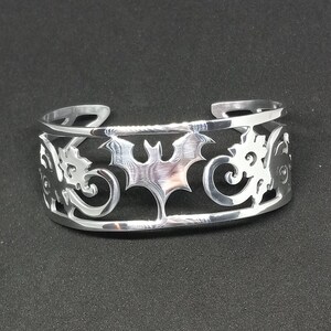Puede incluir: Pulsera de plata con un dise&ntilde;o recortado de un murci&eacute;lago y patrones en espiral.