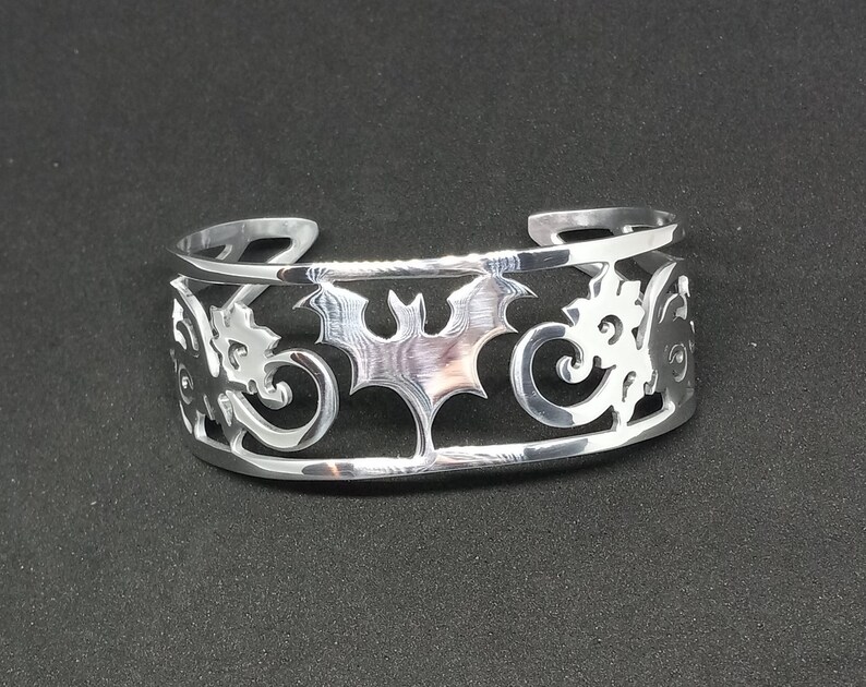 Puede incluir: Pulsera de plata con un dise&ntilde;o recortado de un murci&eacute;lago y patrones en espiral.