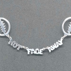 May include: Silver necklace with two circular pendants featuring a stylized lightning bolt design and the words "Not Fade Away".