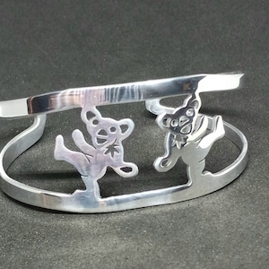 Puede incluir: Pulsera de plata con dos osos bailando recortados. Los osos están en estilo silueta y tienen un diseño de hoja en el pecho.