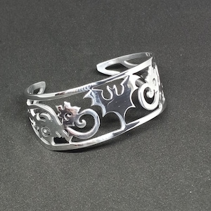 Puede incluir: Una pulsera de plata con un dise&ntilde;o recortado de dragones y espirales.