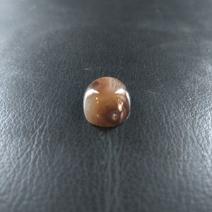 May include: A brown and white agate cabochon with a swirling pattern. The cabochon is smooth and polished.