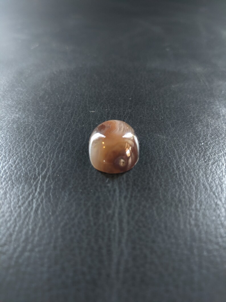May include: A brown and white agate cabochon with a swirling pattern. The cabochon is smooth and polished.