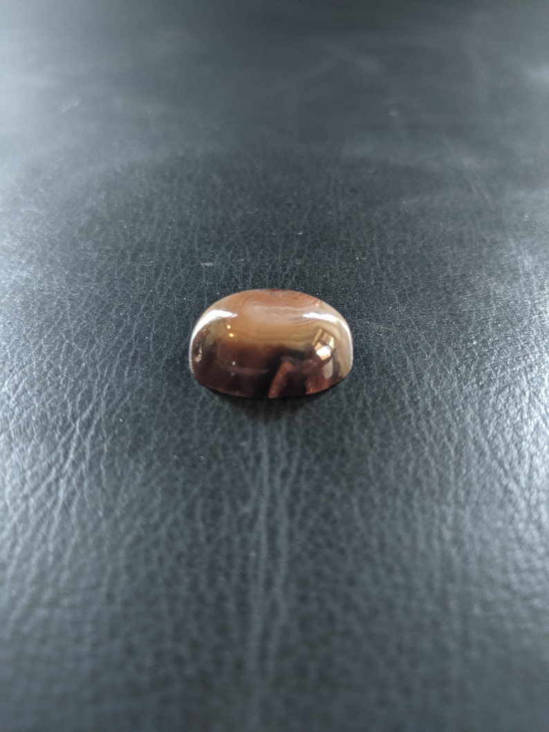 May include: A small, round, dome-shaped object with a smooth, shiny, metallic finish. The object is a light brown color.