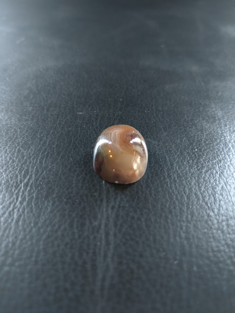 May include: A smooth, oval-shaped agate stone with brown, white, and gray swirling patterns.