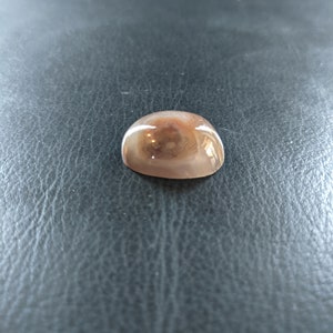 May include: A smooth, round, light brown agate cabochon with a swirling pattern of white and brown.