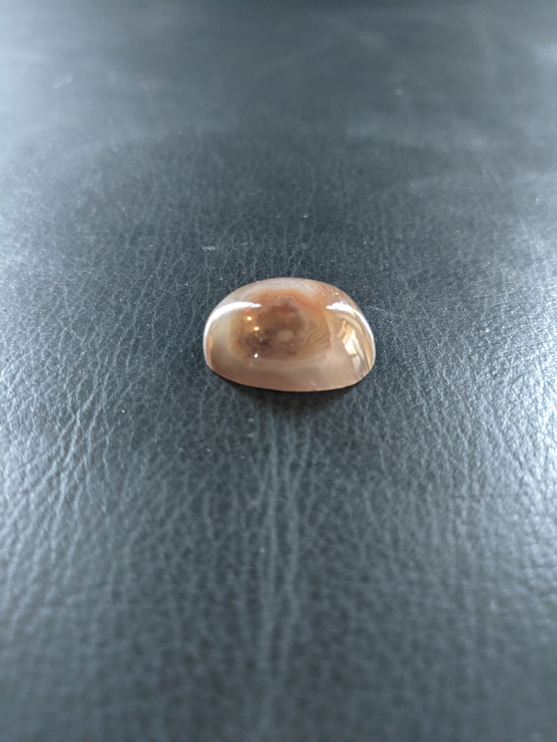 May include: A smooth, round, light brown agate cabochon with a swirling pattern of white and brown.