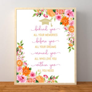 May include: A framed print with a graduation theme. The white background features pink script text: "behind you, all your memories, before you, all your dreams, around you, all who love you, within you, all you need." Floral watercolor art in pink, orange, and green surrounds the text.