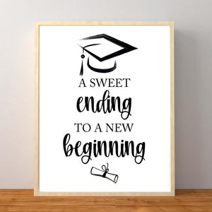 May include: Framed print with a graduation theme. The artwork features a black graduation cap illustration above the words "A sweet ending to a new beginning" in a stylish font. A rolled diploma is at the bottom. The frame is light-colored.