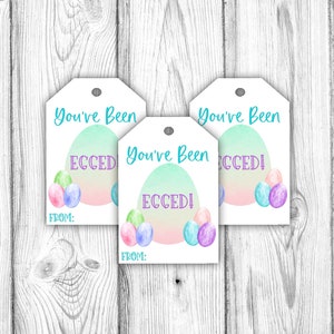 Puede incluir: Tres etiquetas de regalo blancas con un diseño de huevo de acuarela azul pastel y rosa. El texto en las etiquetas dice "You've Been Ecceded!" con las palabras "From:" en la parte inferior de cada etiqueta.