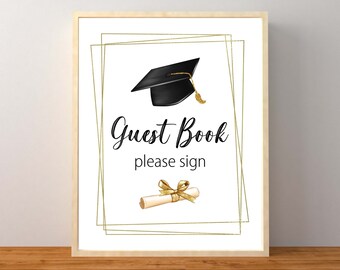 May include: A white sign with a gold frame and a black graduation cap with a gold tassel. The sign says "Guest Book please sign" and has a gold ribbon and a diploma scroll.