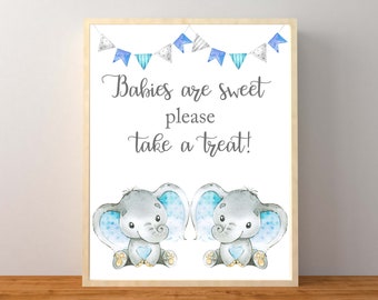 May include: A baby shower sign with two gray elephants with blue ears and a blue heart on their chests. The sign says "Babies are sweet please take a treat!" with blue and white bunting above the elephants.
