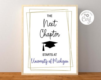 May include: A white sign with gold frames and black text that reads "The Next Chapter Starts At University of Michigan". A black graduation cap is in the center of the sign.